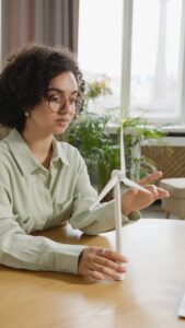 Une jeune femme concentrée étudie un modèle d'éolienne à l'intérieur, mettant en avant les énergies renouvelables et l'éducation.