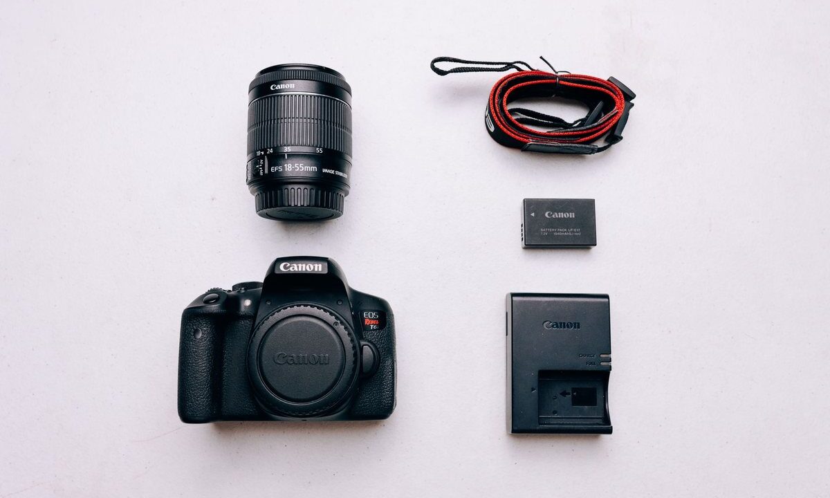 Un appareil photo Canon, objectif, batterie, chargeur et câble sur fond blanc