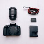 Un appareil photo Canon, objectif, batterie, chargeur et câble sur fond blanc