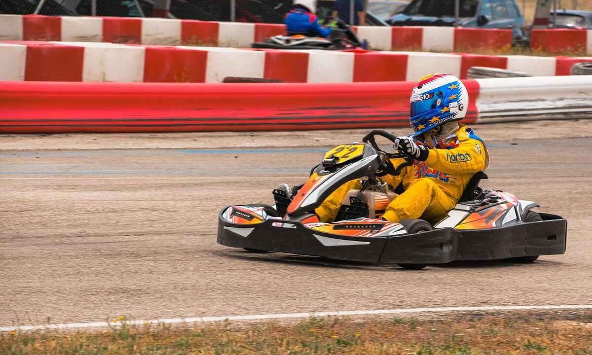 Pilote de kart en action sur circuit, barrières rouges et blanches, casque coloré, tenue de course
