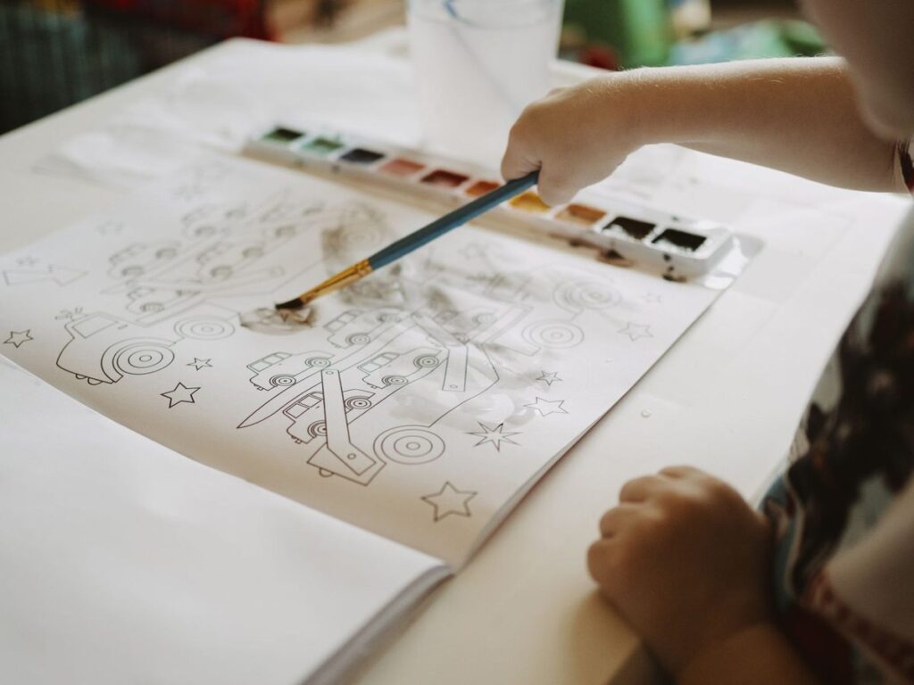 Enfant coloriant un dessin avec des aquarelles sur une table
