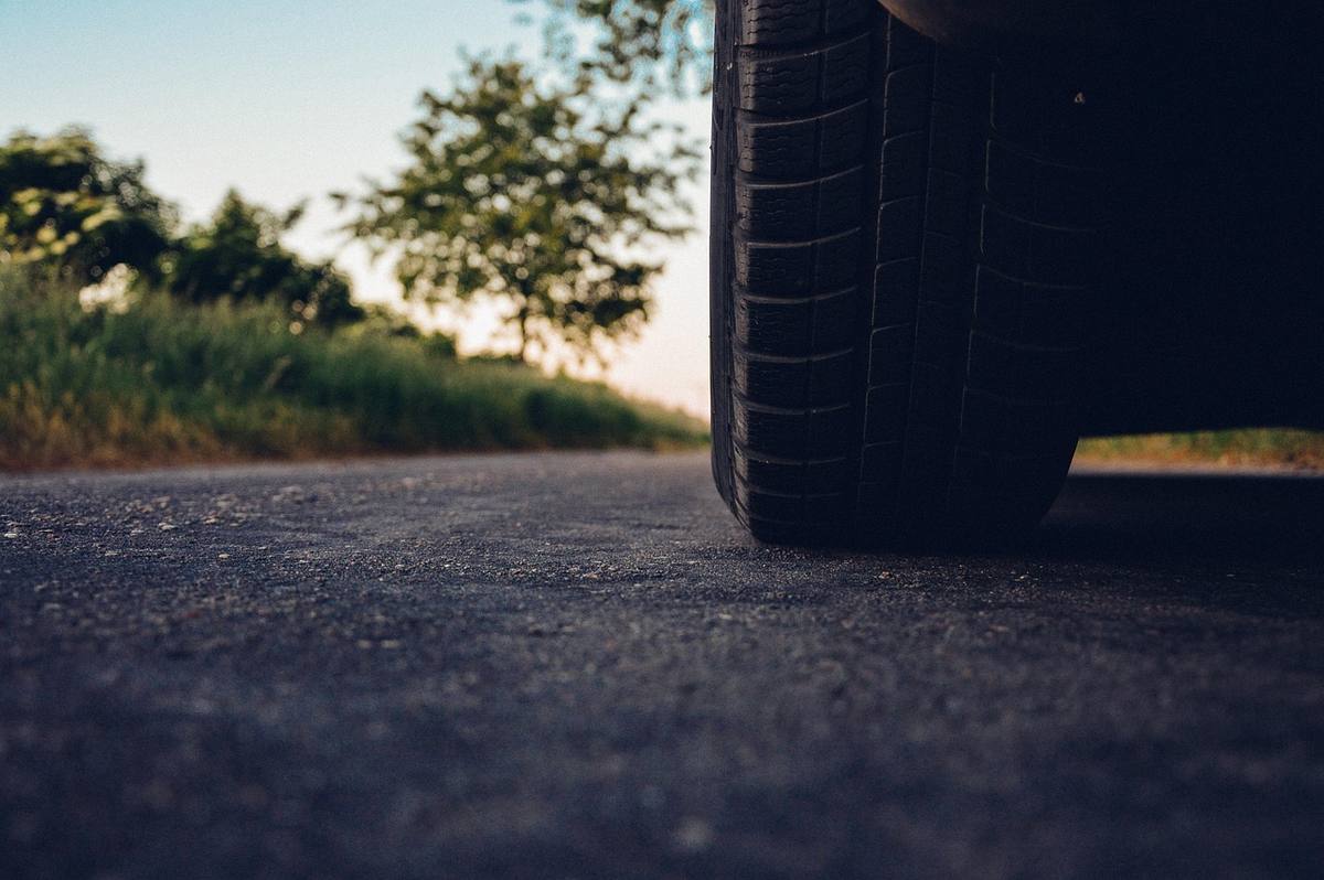 Un pneu de voiture posé sur une route asphaltée, feuillage verdoyant