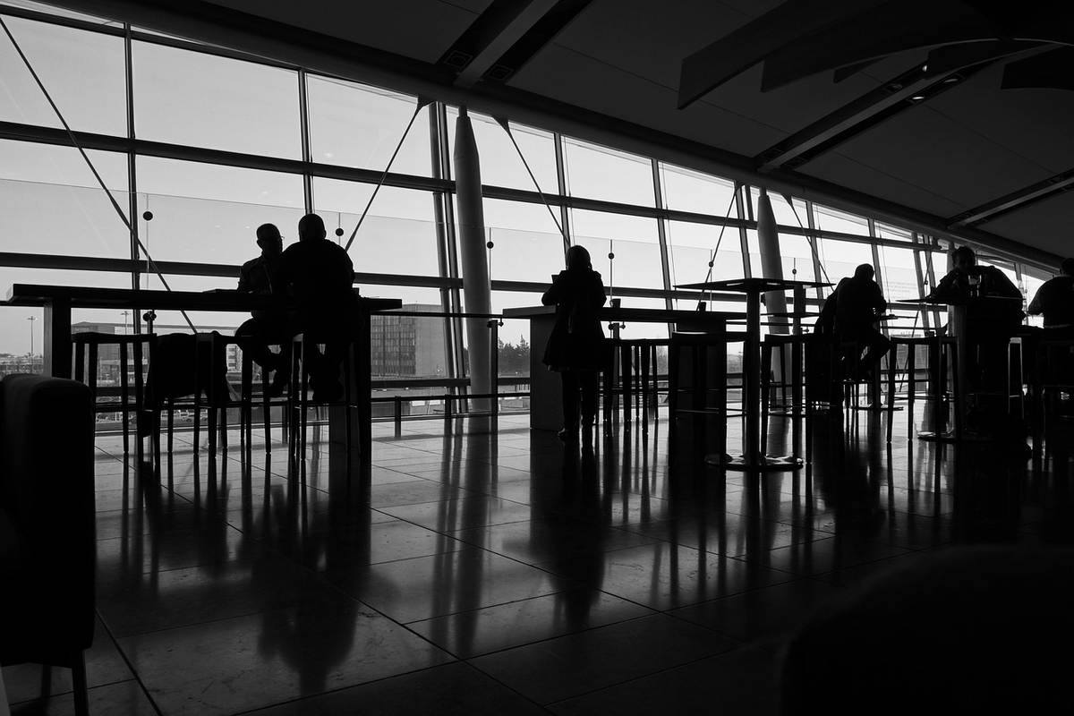 Personnes en silhouette dans un terminal d'aéroport avec grandes baies vitrées et vue dégagée