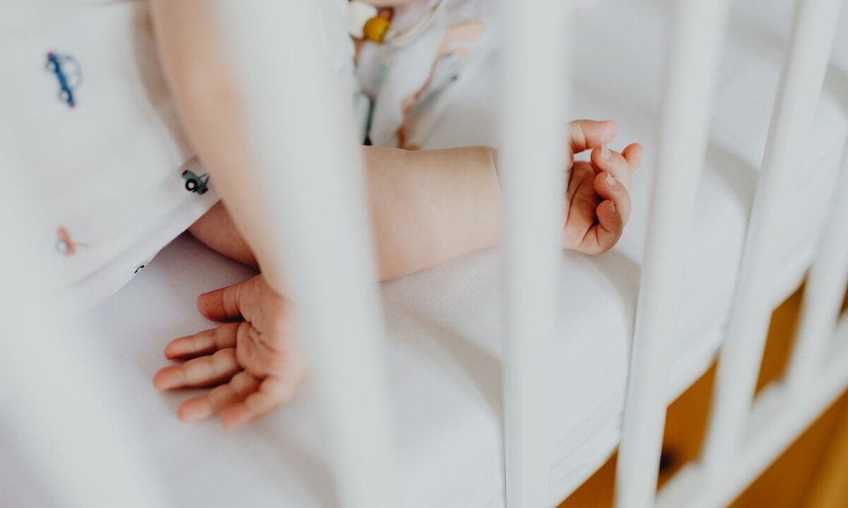 Bras et mains d'un enfant sur un lit blanc avec des barreaux, en train de jouer
