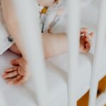 Bras et mains d'un enfant sur un lit blanc avec des barreaux, en train de jouer