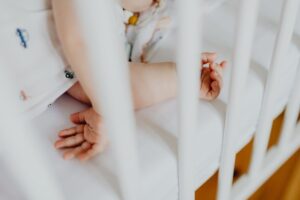 Bras et mains d'un enfant sur un lit blanc avec des barreaux, en train de jouer