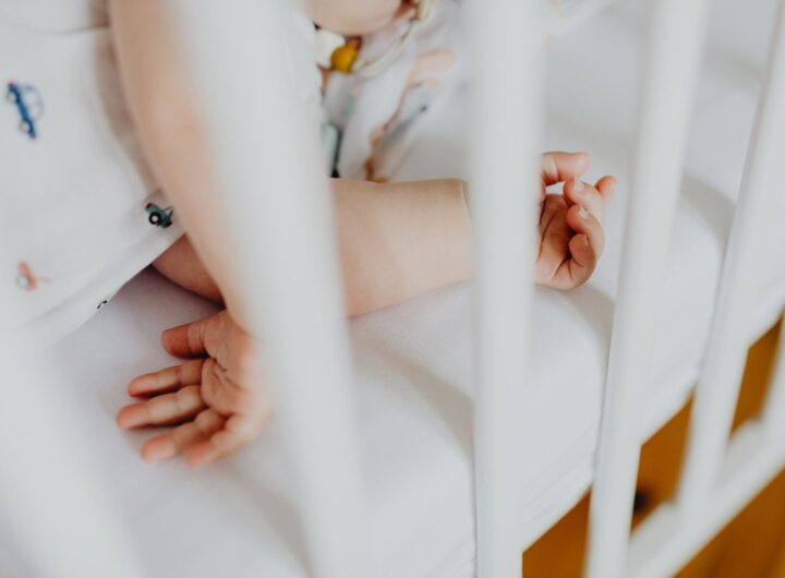 Bras et mains d'un enfant sur un lit blanc avec des barreaux, en train de jouer