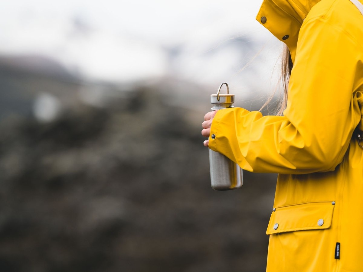 Une personne en veste jaune tient une gourde devant un décor montagneux Une personne en veste jaune tient une gourde devant un décor montagneux