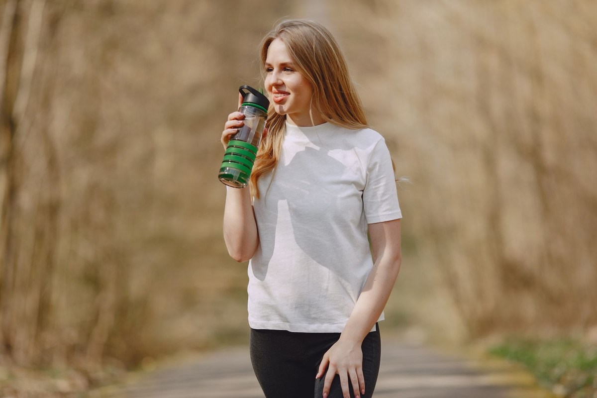 Une femme boit depuis une gourde verte sur un sentier Une femme boit depuis une gourde verte sur un sentier