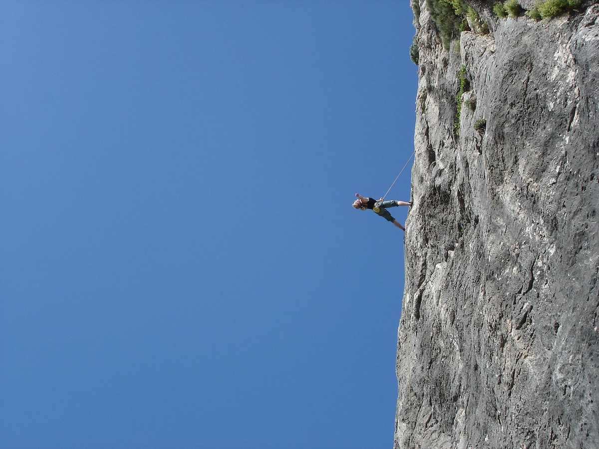 Personne en escalade sur une falaise rocheuse, ciel bleu sans nuages