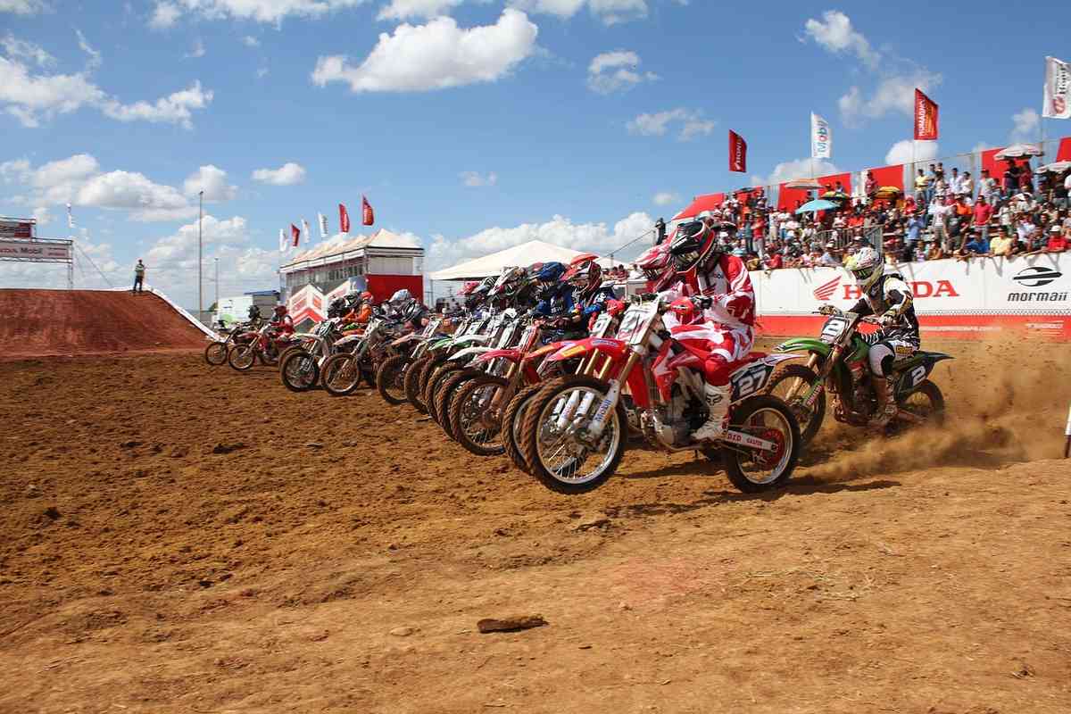 Des motocyclistes en tenue de course démarrent sur un circuit boueux