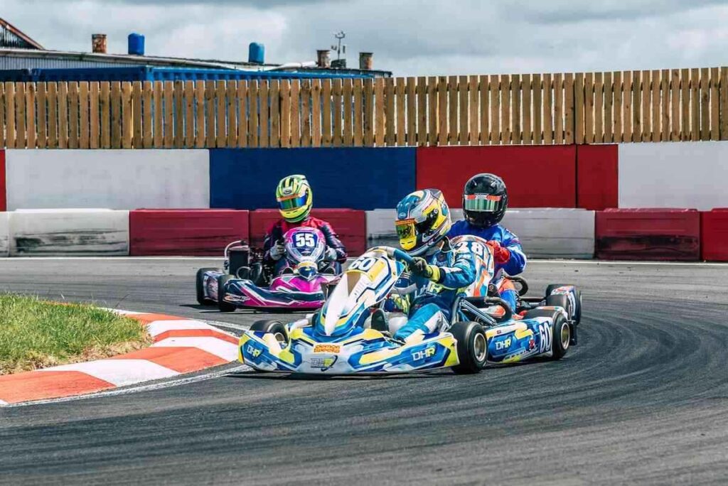 Trois karts dérapent en virage sur circuit, pilotes en casques colorés