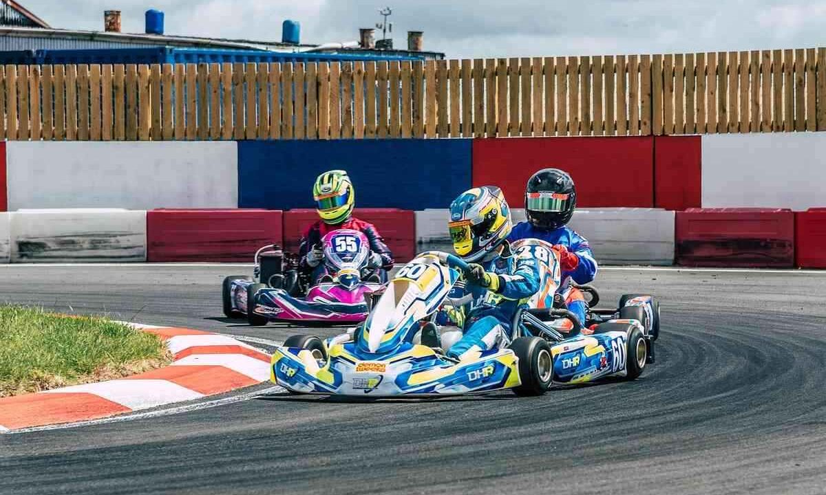 Trois karts dérapent en virage sur circuit, pilotes en casques colorés